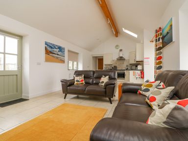 A living room with two brown leather sofas and patterned cushions an orange rug and a kitchen area at Pen Tewan in Sennen