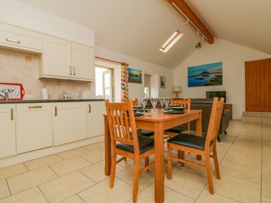 A kitchen dining area with wooden table and chairs set with glasses and plates at Pen Tewan in Sennen