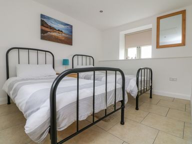 A bedroom with two single beds with metal frames a window with a blind and a wall mirror at Pen Tewan in Sennen