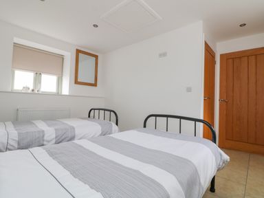 A bedroom with two single beds with striped bedding a window with a blind and a framed mirror on the wall at Pen Tewan in Sennen