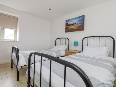 A bedroom with two single beds a wooden nightstand with a blue lamp and a landscape painting on the wall at Pen Tewan in Sennen