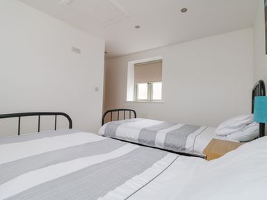 A bedroom with two single beds with striped bedding a small window and a bedside table at Pen Tewan in Sennen