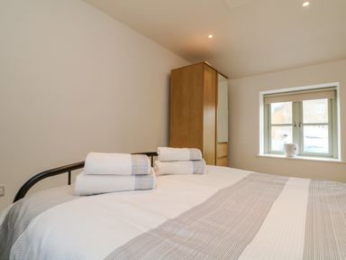 A bedroom with a bed, folded towels on the bed, a wardrobe, and a window at Pen Tewan in Sennen