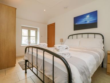 A bedroom with a metal bed frame white bedding folded towels on the bed wooden wardrobe and nightstand a window and a door at Pen Tewan in Sennen