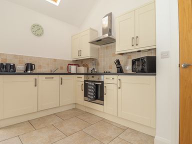 A kitchen with beige cabinets tiled backsplash and floor with appliances at An Gwel in Sennen