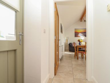 A hallway leading to a dining area with a wooden table and chairs a black leather sofa a floor lamp and wall art at An Gwel in Sennen