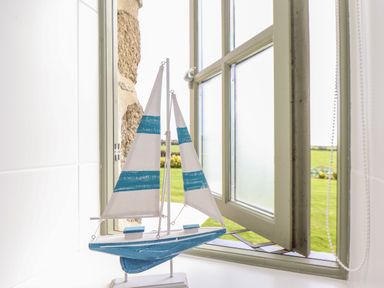 A model sailboat with blue and white sails on a windowsill with an open window and a green field outside at An Gwel in Sennen