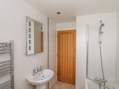 A bathroom with a sink hat has two taps and a mirror above it with a wooden door and a bathtub with a shower at An Gwel in Sennen