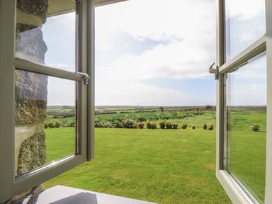 A view of green fields and shrubs seen through an open window at An Gwel in Sennen