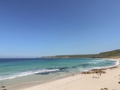 A sandy beach with people near the shore and turquoise ocean water at An Gwel in Sennen