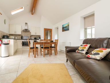 A kitchen and dining area with a wooden dining table and chairs next to a brown sofa with patterned cushions at An Gwel in Sennen