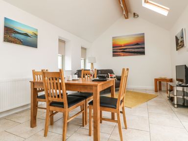 A dining area with wooden table and chairs next to a living space with a sofa and television at An Gwel in Sennen