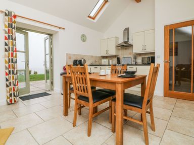 A kitchen with wooden dining table and chairs near a glass door and a skylight at An Gwel in Sennen