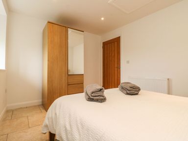 A bedroom with a bed covered in white linens with two folded towels on top a wooden wardrobe with a mirror and a closed wooden door at An Gwel in Sennen