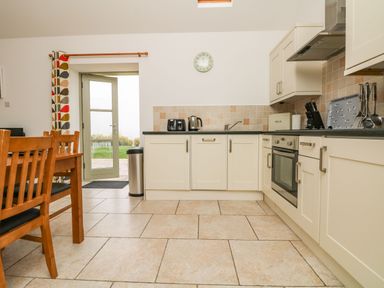 A kitchen with cream cabinets a wooden dining table and chairs and a door leading outside at An Gwel in Sennen