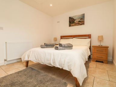 A bedroom with a double bed bedside tables lamps towels on bed and a painting on the wall at An Gwel in Sennen