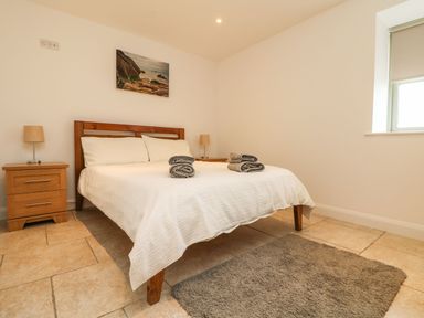 A bedroom with a wooden bed white bedding bedside tables with lamps and a gray rug on tiled floor at An Gwel in Sennen