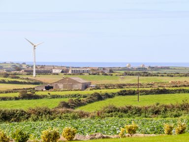 A rural landscape with fields barns a wind turbine and the sea in the background at An Garth in Sennen