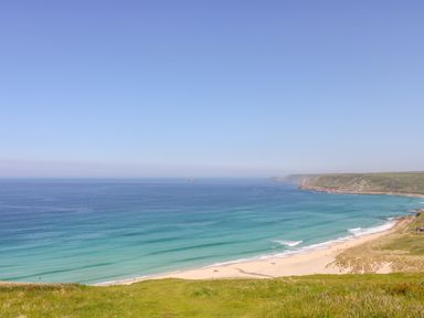 A coastal scene with a sandy beach and grassy cliff at An Garth in Sennen