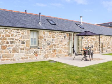 An outdoor patio area with a table and chairs under an umbrella next to a stone house with a lawn at An Garth in Sennen