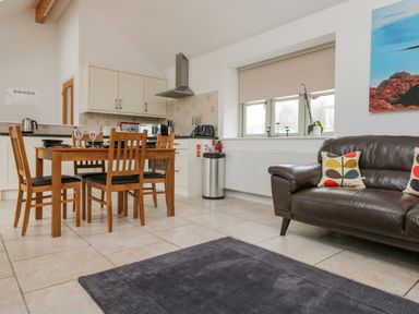 A kitchen and dining area with a wooden table and chairs and a leather sofa at An Garth in Sennen