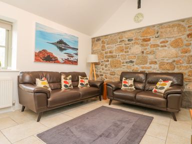 A sitting room with two brown leather sofas cushions on a rug and a stone feature wall at An Garth in Sennen