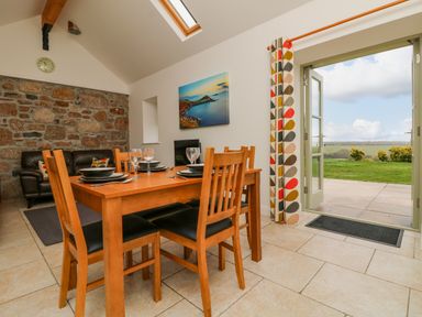A dining area with a wooden table set for four near an open door leading to a patio with a green lawn at An Garth in Sennen