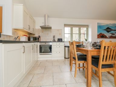 A kitchen with white cabinets a stainless steel oven a wooden dining table with chairs and a window with a view at An Garth in Sennen