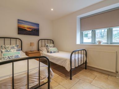 A bedroom with two single beds and a nightstand under a painting at An Garth in Sennen