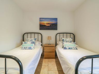 A bedroom with two single beds and a wooden nightstand with a lamp at An Garth in Sennen
