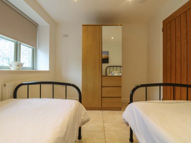 A bedroom with two single beds a wooden wardrobe with a mirror a window with a blind and a door at An Garth in Sennen