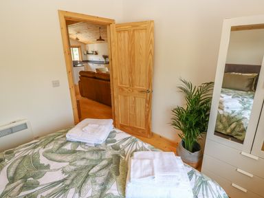A bedroom with a bed covered with a leaf patterned duvet and folded towels at Willow Lodge in St Florence