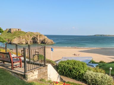A sandy beach with people near the water and a rocky hill with a fort overlooking the sea at Willow Lodge in St Florence