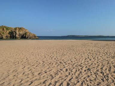 A sandy beach with rocks on the left and sea under a clear sky at Willow Lodge in St Florence