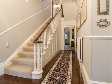 A hallway with carpeted stairs a patterned runner rug framed pictures and mirrors on the wall at Holcombe House in Torquay
