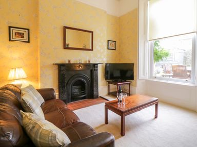 A living room with a leather sofa pillows a wooden coffee table with wine glasses and bottle a television on a side table a fireplace and a large window at Holcombe House in Torquay