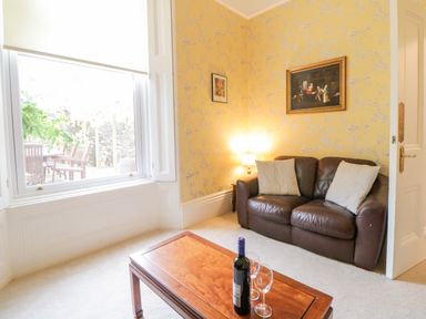 A sitting room with a brown leather sofa two cushions a wooden coffee table with wine bottle and glasses yellow wallpaper Holcombe House Torquay