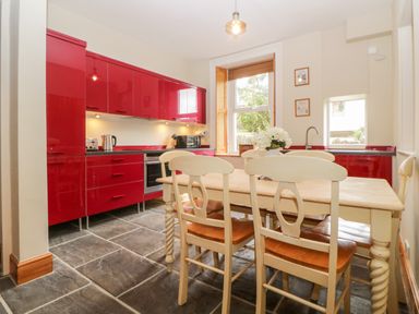 A kitchen with red cabinets a wooden dining table with chairs and a window at Holcombe House in Torquay