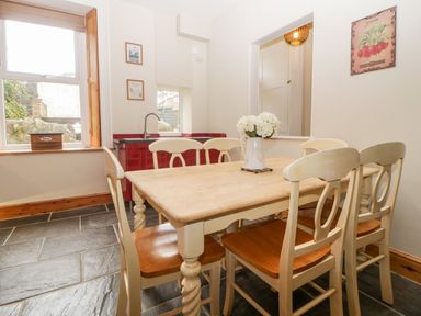 A dining area with a wooden table and six chairs next to a kitchen counter with a sink at Holcombe House in Torquay