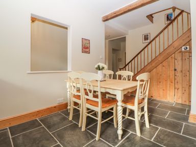 A dining area with a wooden table and six chairs next to a staircase with wooden railing at Holcombe House in Torquay
