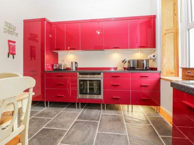 A kitchen with red cabinets a stainless steel oven countertop appliances and a window at Holcombe House in Torquay