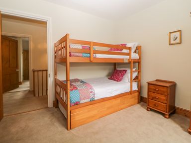 A bedroom with a wooden bunk bed featuring colorful bedding a small wooden chest of drawers and an open door at Holcombe House in Torquay