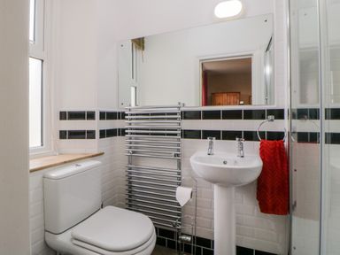 A bathroom with a toilet, pedestal sink, wall-mounted mirror, towel rack, and shower enclosure at Holcombe House in Torquay