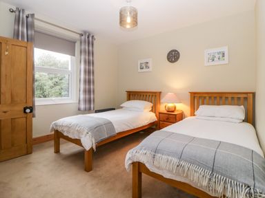 A bedroom with two single beds a wooden door a window with checked curtains and a bedside table with a lamp at Holcombe House in Torquay