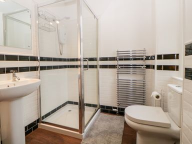 A bathroom with a glass shower enclosure a white pedestal sink a toilet a towel radiator and a floor mat at Holcombe House in Torquay