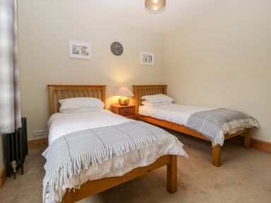 A bedroom with two single wooden beds with white bedding and gray throws with a wooden nightstand with a lamp between them at Holcombe House in Torquay