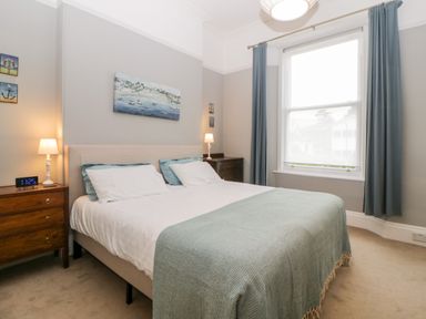 A bedroom with a double bed, bedside tables with lamps, wall paintings, and a large window with curtains at Holcombe House in Torquay