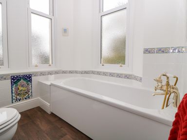A bathroom with a white bathtub and gold faucet under frosted windows at Holcombe House in Torquay