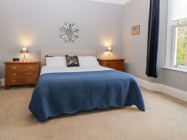 A bedroom with a bed covered in a blue blanket two wooden bedside tables with lamps and a window with dark curtains at Holcombe House in Torquay