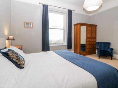 A bedroom with a bed bedside table lamp wooden wardrobe and blue armchair at Holcombe House in Torquay